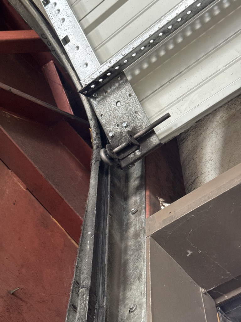  Garage door track repair showing a damaged vertical track and misaligned garage door roller.