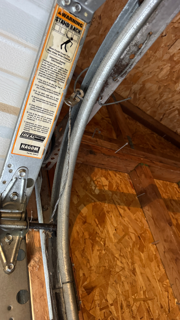  Garage door track repair showing a damaged vertical track and misaligned garage door roller. 