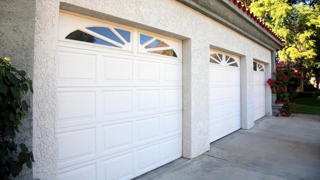 Three white garage doors with arched window inserts on a stucco home, used for a new garage door cost guide for homeowners