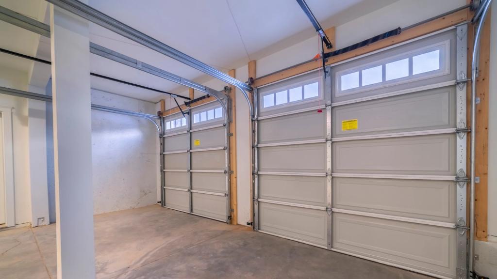 Residential garage in Wisconsin with two white sectional garage doors and visible tracks, rollers, hinges, and overhead hardware